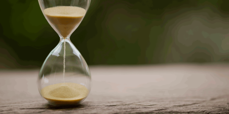 Sand clock , Hourglass as time passing on green nature background - Image credit - iStock- 1342058281