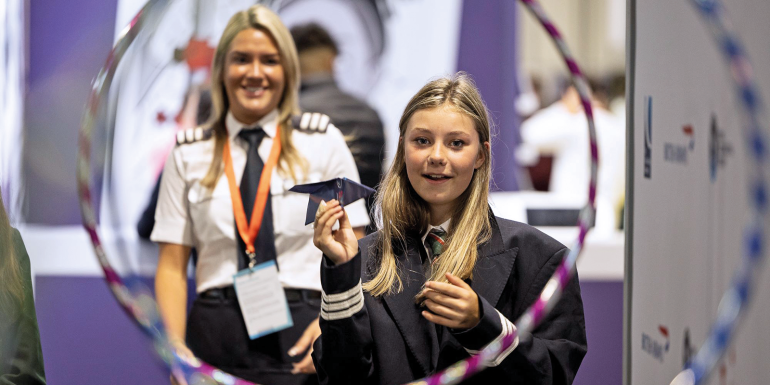 pilot watches as student attempts to fly paper plane through obstacle course