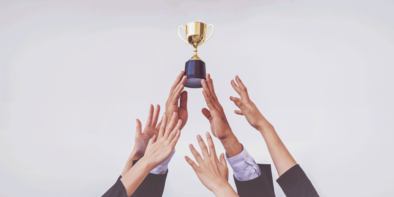 Hand holding trophy with others reaching for it. credit_istock-2165195635.