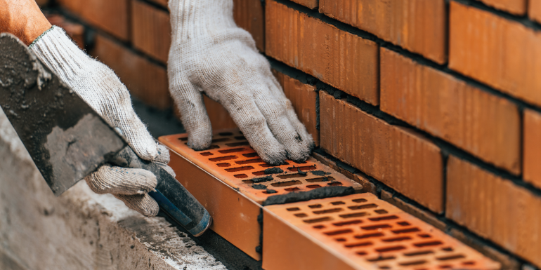 Worker or mason hands laying bricks close up. Bricklayer works at brick row.CREDIT_shutterstock_2179221401