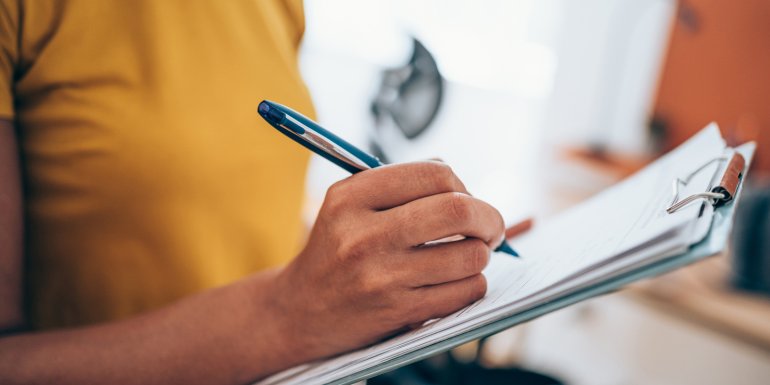 woman hand writing on clipboard with a pen. Credit_iStock-1434437996