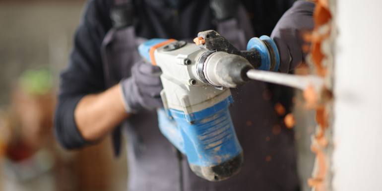 Close up of a construction worker using rotary hammer to wreck wall in a house under renovation.Image credit | Shutterstock