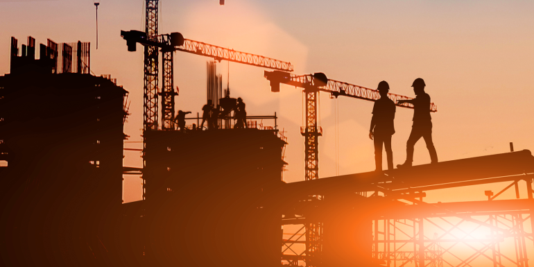 Silhouette Two engineers consult and inspect high-rise construction work over blurred industry background with Light fair.CREDIT_shutterstock_1489933823