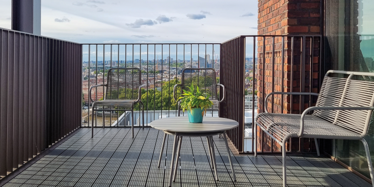A spacious balcony features two chairs and a small table with a potted plant. CREDIT_istock-2194777643