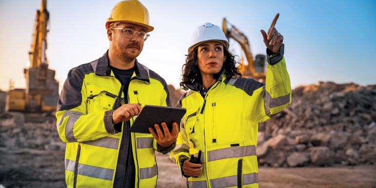 Caucasian Male Civil Engineer Talking To Hispanic Female Inspector And Using Tablet Computer On Construction Site of New Building. Real Estate Developers Discussing Business, Excavators Working.Image credit | Shutterstock