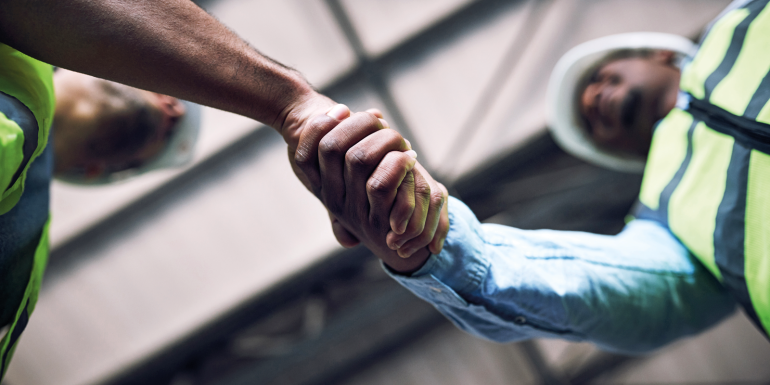 Shot of two builders shaking hands at a construction site stock photo.CREDIT_istock-1326873286