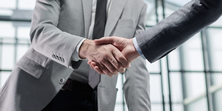 Two men shaking hands in a business setting.CREDIT_shutterstock_2726571525