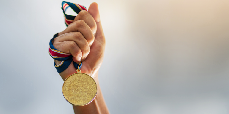 Hand holding gold medal on sky background, The winner and successful concept.CREDIT_shutterstock_1436517377