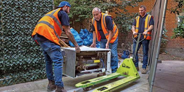 Workers moving heavy machinery with pallet jack.CREDIT_Thomas-Graham