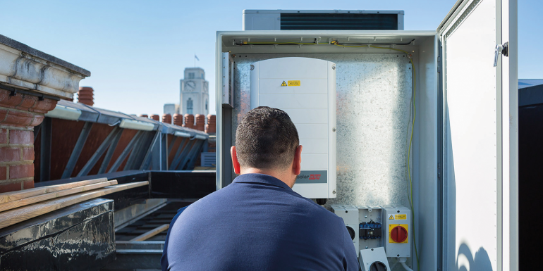 Technician inspecting rooftop solar power inverter.CREDIT_Thomas-Graham