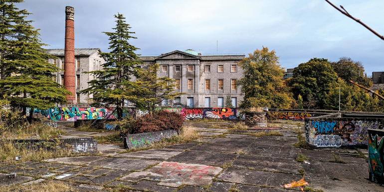 Derelict boarded up buildings viewed across graffiti covered walls of abandoned vacant car park roof garden downtown.credit_istock-2231446932