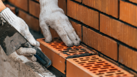 Worker or mason hands laying bricks close up. Bricklayer works at brick row.CREDIT_shutterstock_2179221401