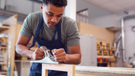 Male Student Studying For Carpentry Apprenticeship At College Using Wood Plane. CREDIT_istock-1218972142.png 
