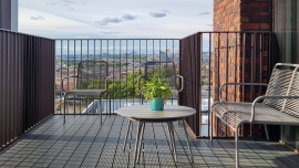 A spacious balcony features two chairs and a small table with a potted plant. CREDIT_istock-2194777643