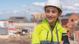 Portrait of smiling young woman builder in bright safety gear and hard hat at construction site. Image credit | istock