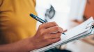 woman hand writing on clipboard with a pen. Credit_iStock-1434437996